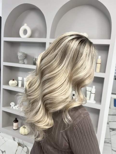 Blond ondulat în fața celor două nișe în arcadă cu produse, pe partea de coafor